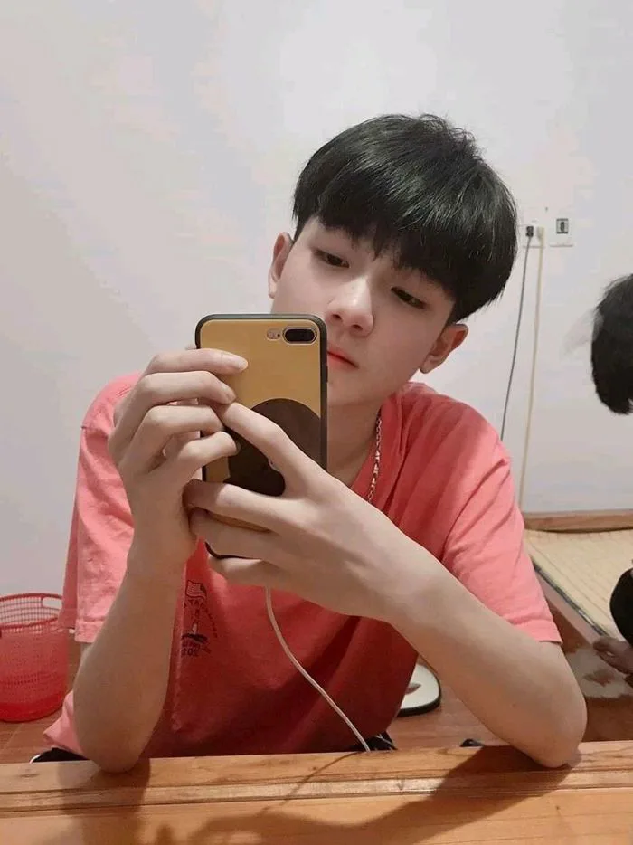 Anh áo hồng ngồi trên giường để chụp ảnh trước gương